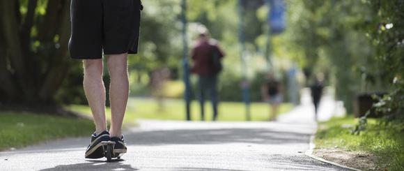 Student using a scooter ona path.  Other students are in the distance walking towards him