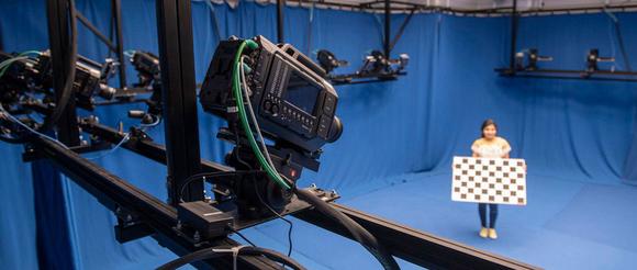 A girl surrounded by cameras is holding a chequered board to configure them.