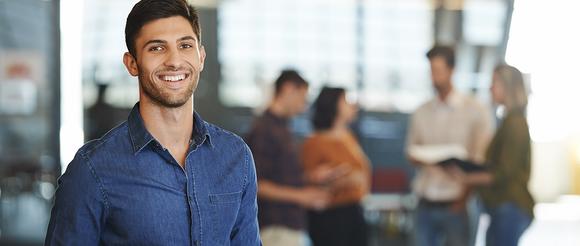 Man looking towards the camera.  Work colleagues are out of focus in the background.