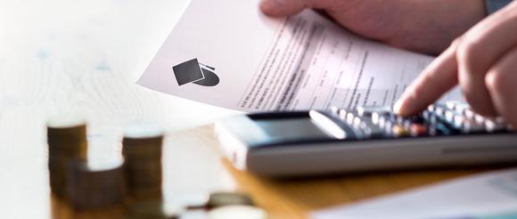 A student using a calculator whilst holding an application form.  There are coins in the foreground.