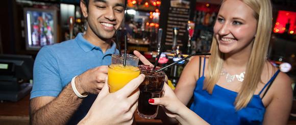 Students clinking glasses in front of a bar.