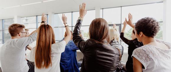 A group of students raising their hands ready to make their point in a discussion.