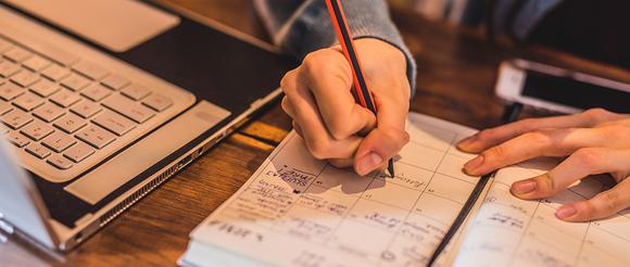 A student copying his timetable into a diary on his desk.