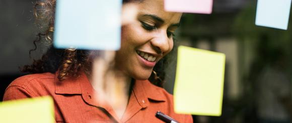 Female looking down writing on a post-it note.