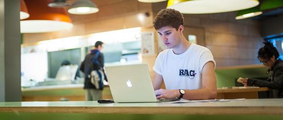 Student sat in Young's Kitchen on a laptop