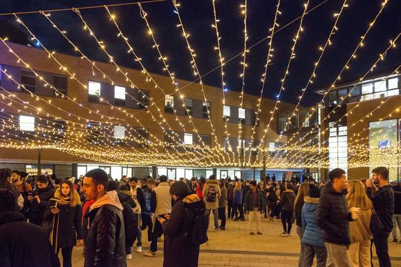 A wide photo of the festive piazza lights. Lots of students are standing underneath them