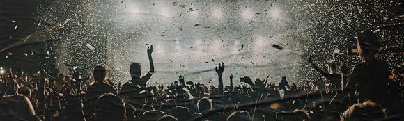 A photo showing a crowd at a concern. They are all looking towards a brightly lit stage