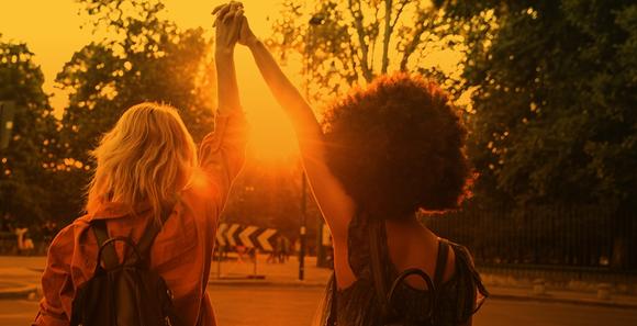  A sunset casts a golden hue as two women walk hand in hand down a street, symbolising friendship and connection.